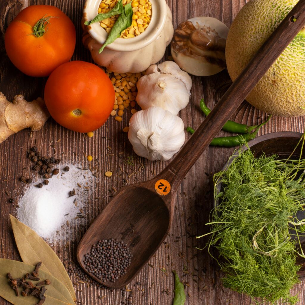 A flat lay of fresh herbs, spices, and vegetables on a rustic wooden surface.