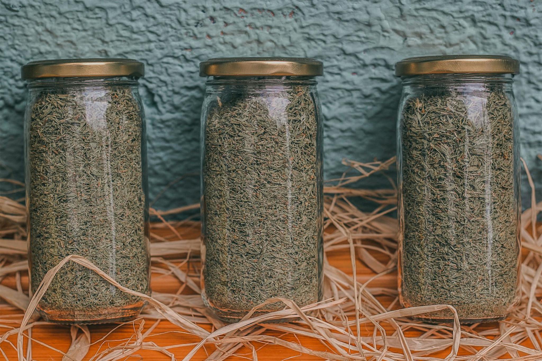 Close-up of dried herbs in three glass jars on a rustic wooden surface.