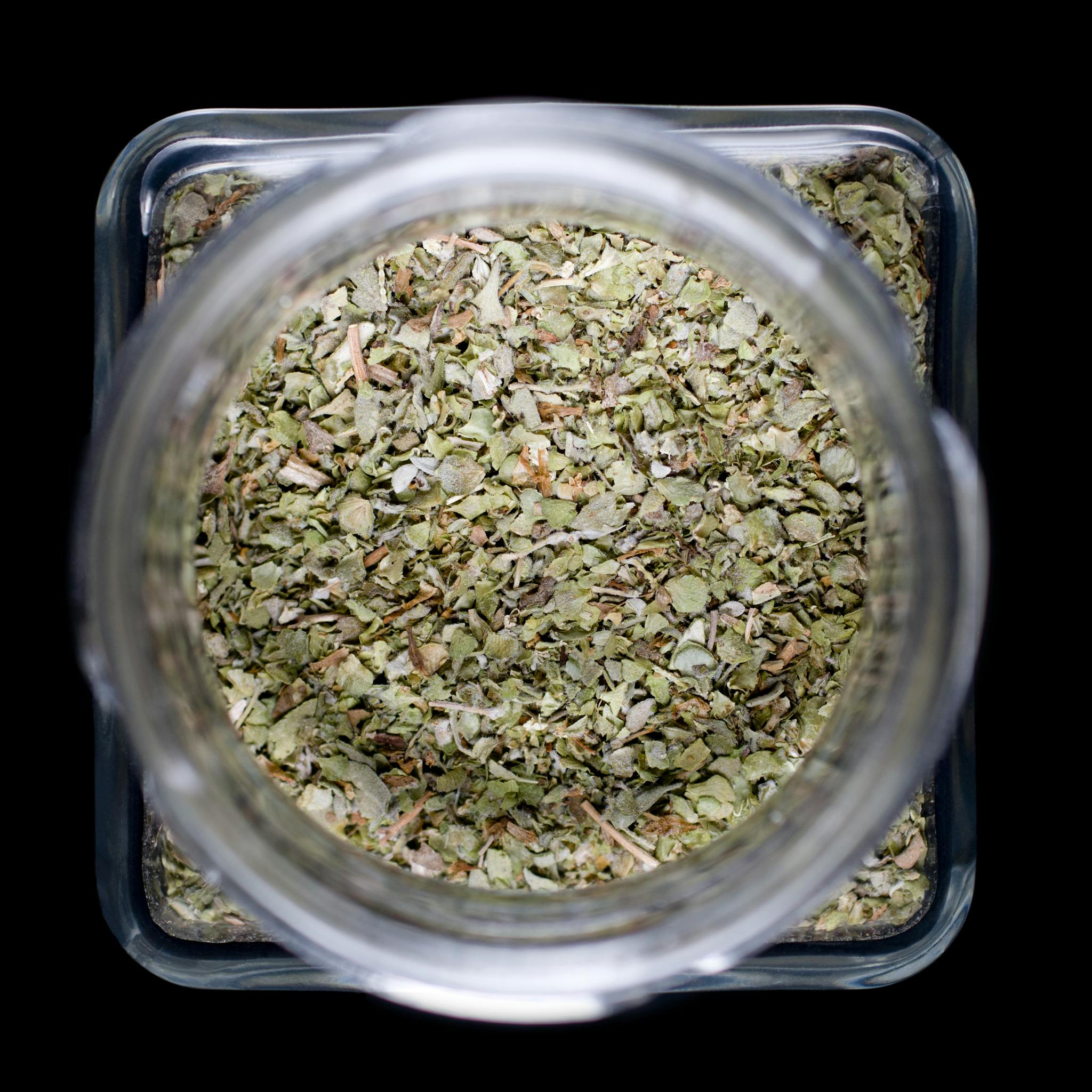Herbs stored in a clear jar showcasing dried marjoram leaves from above.