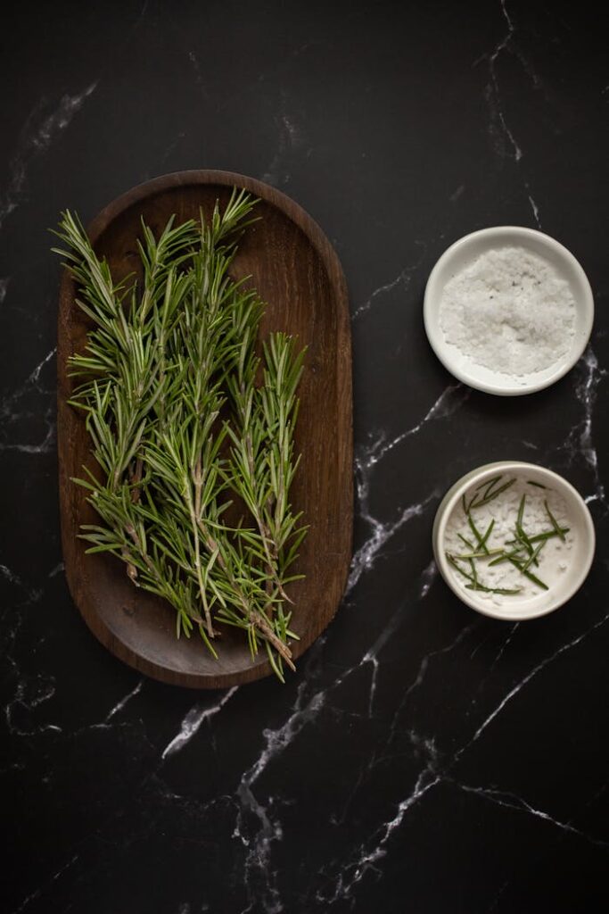 Top view of fresh rosemary with sea salt on dark marble surface. Perfect for culinary and herbal themes.