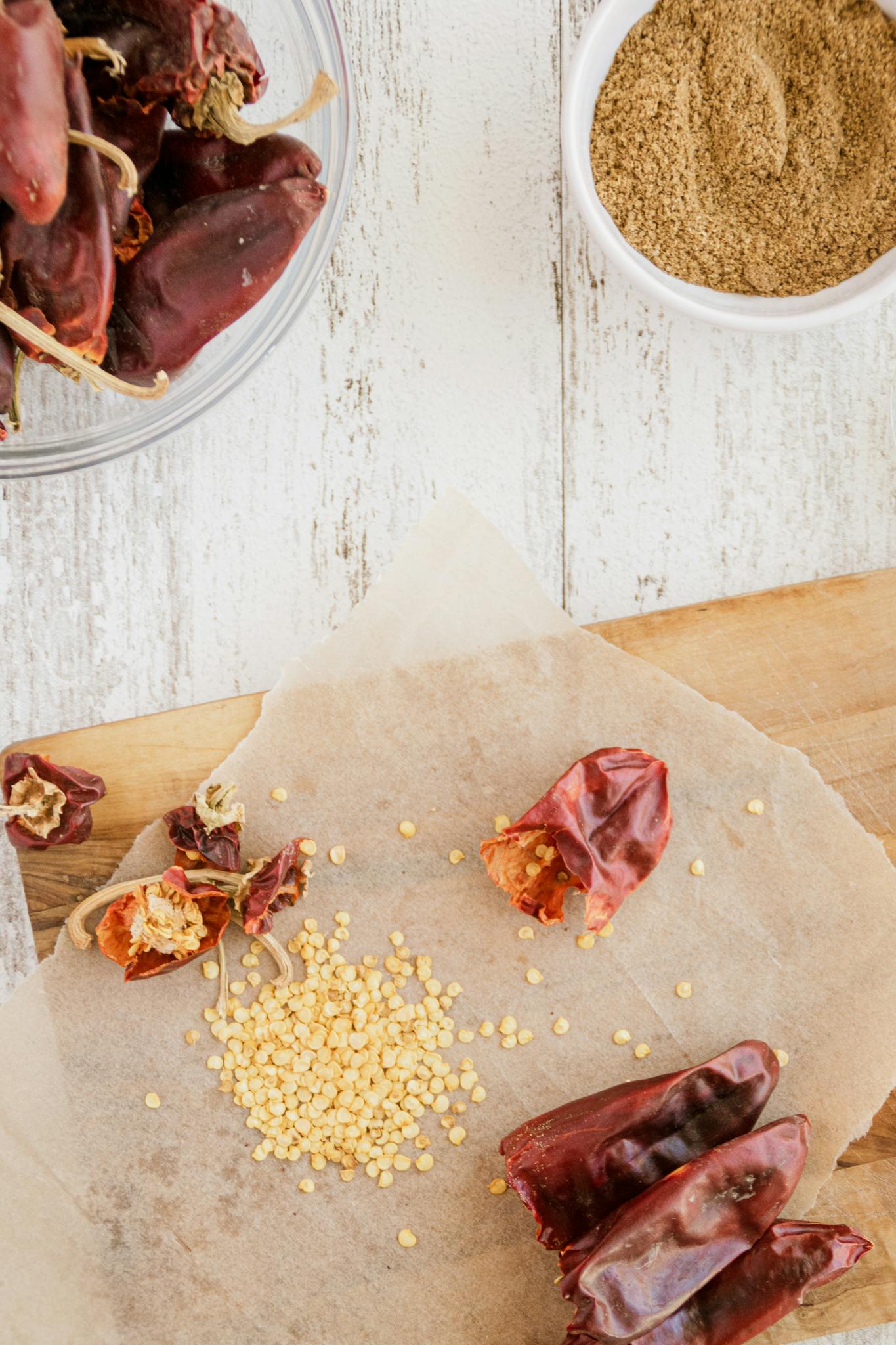 Top view of dried red peppers, seeds, and spices on parchment paper for culinary inspiration.
