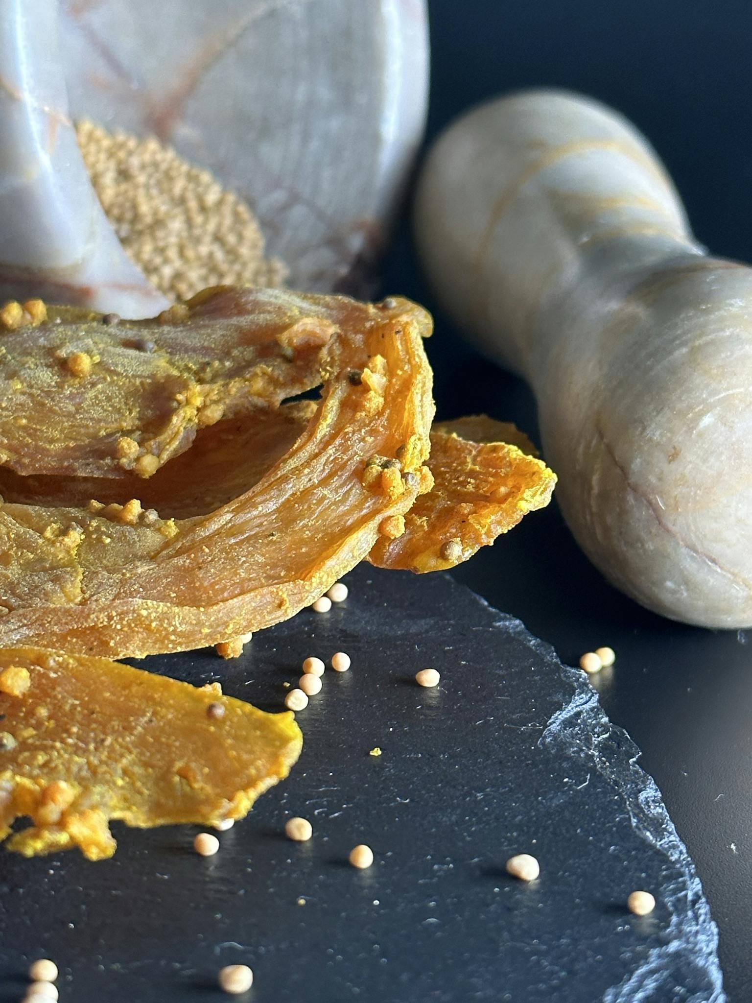 Vibrant dried mango slices with mustard seeds on a slate surface.